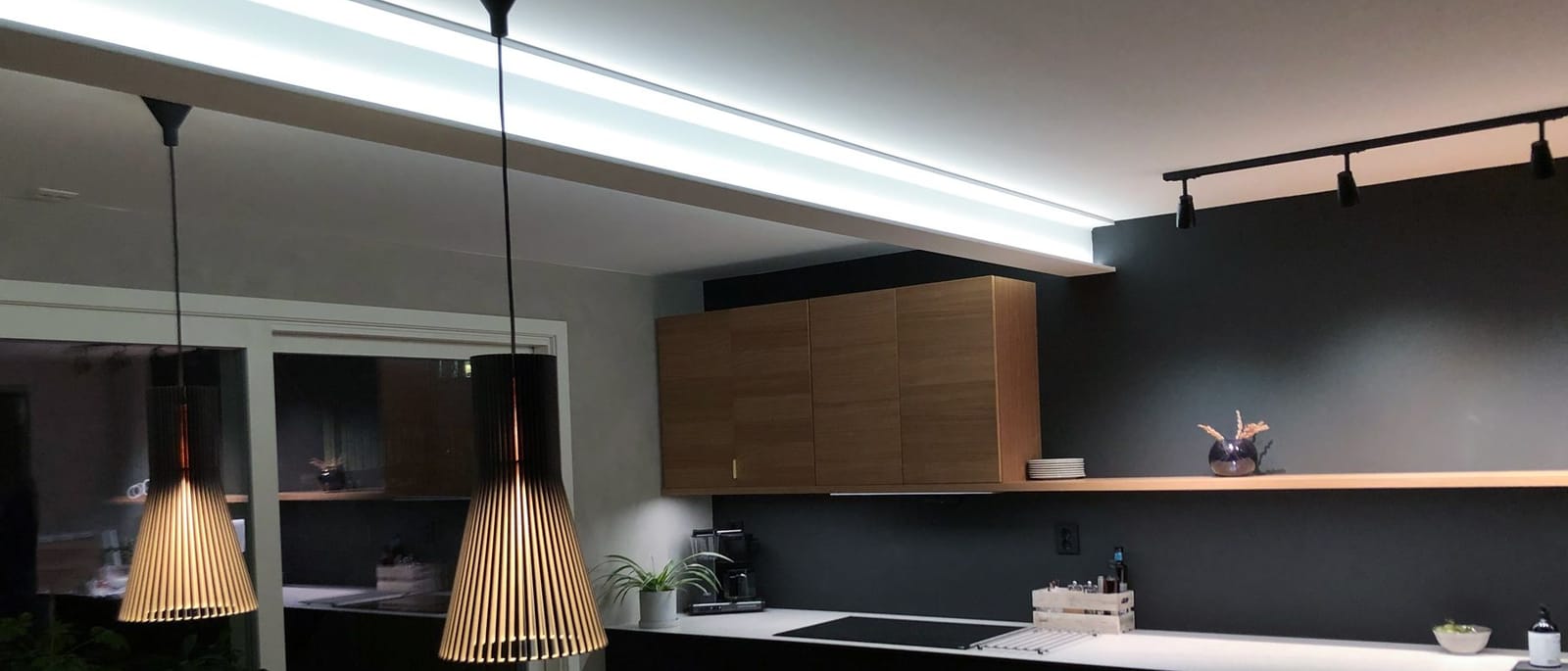 Kjøkken med LED-profil i taket, to pendler over spisebordet og en skinne med spotter over arbeidsbenken.