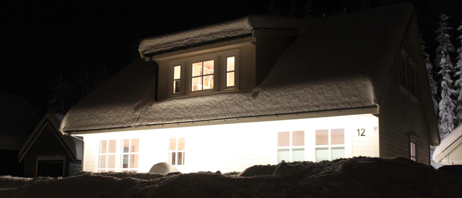 Hus med snø på taket og LED-lys langs takutstikket som lyser opp veggen en mørk vinterkveld.