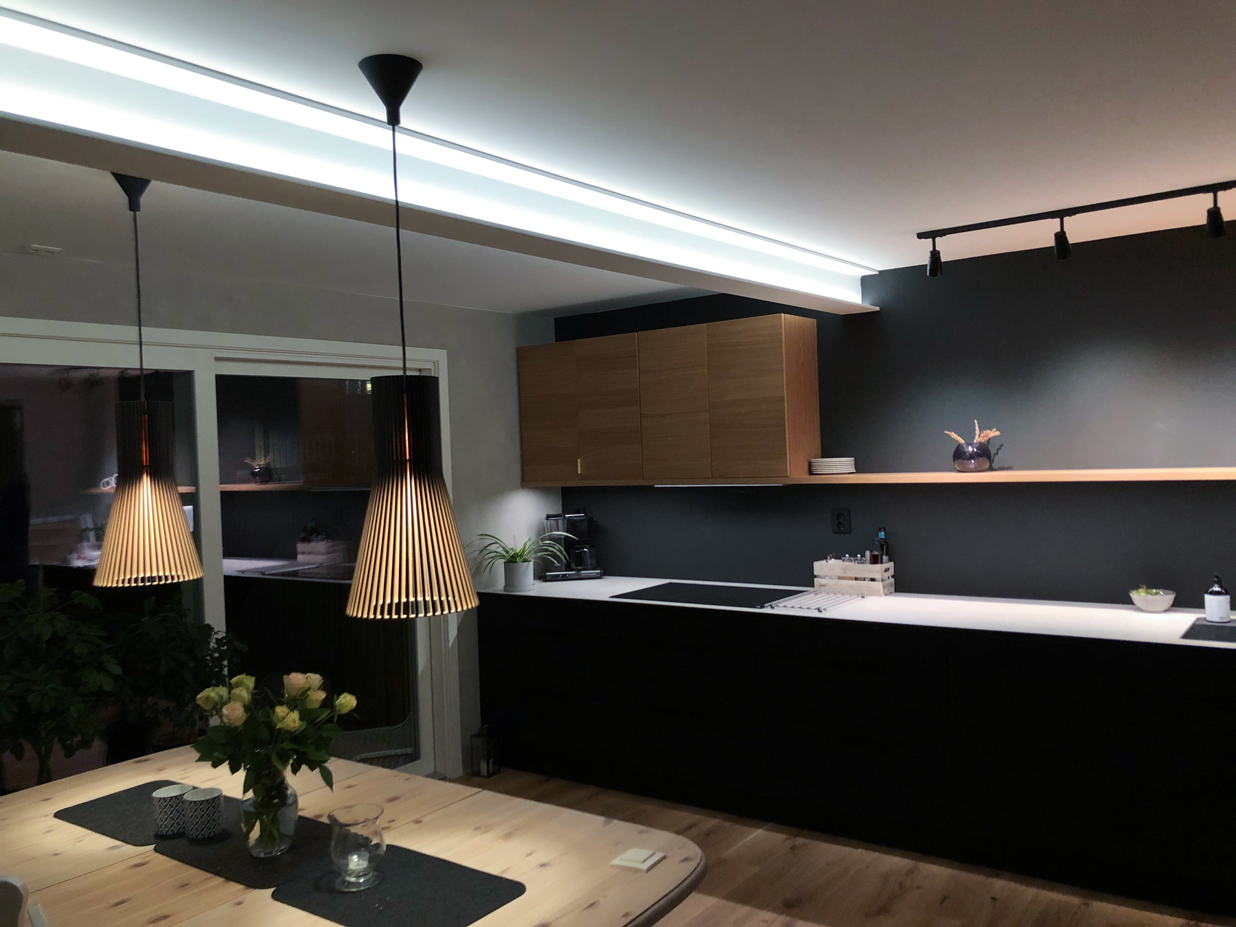 Kjøkken og spiseområde med LED-lysstripe i taket, sorte pendellamper og skinnespotter